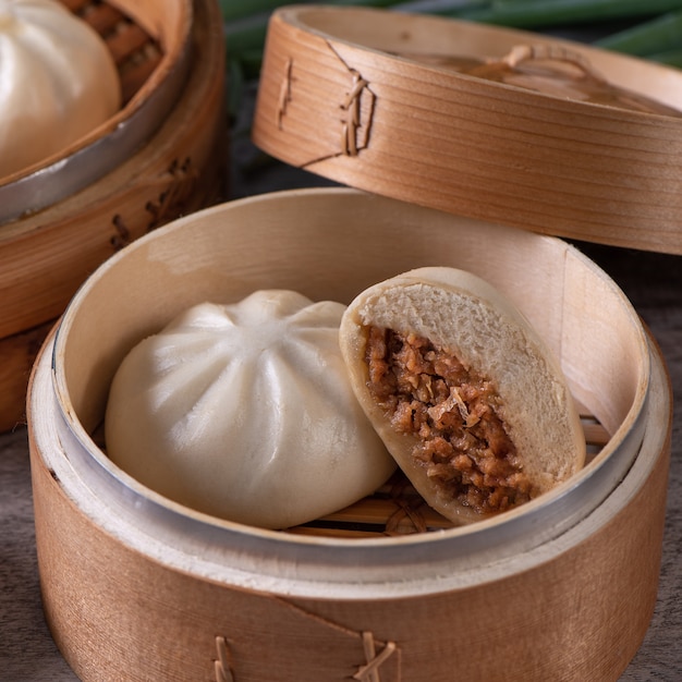 Köstlicher Baozi, chinesisches gedämpftes Fleischbrötchen ist fertig zum Essen auf Servierplatte und Dampfgarer, Nahaufnahme, Produktdesignkonzept für Kopienraum.