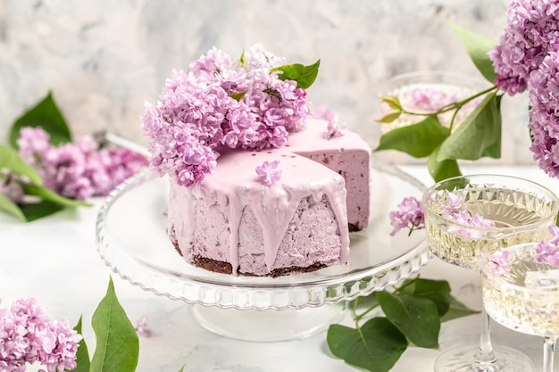 Köstlicher Beeren-Mousse-Kuchen mit Champagner-Weinstrauß aus lila blühenden Fliedern Französische Küche Postkartenhintergrund