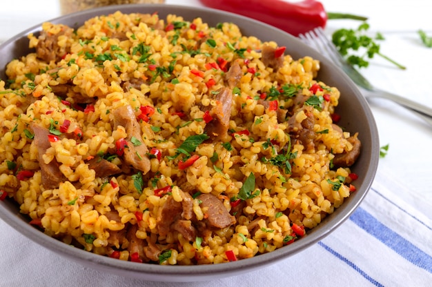 Köstlicher Bulgur mit Gemüse, Fleisch und Gemüse auf einem weißen Holztisch.