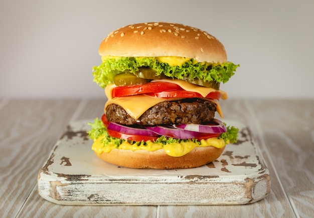 Köstlicher Burger mit Fleisch, geschmolzenem Käse, tropfender Soße und Gemüse auf weißem rustikalem Hintergrund. Frisch zubereiteter leckerer Hamburger, Nahaufnahme