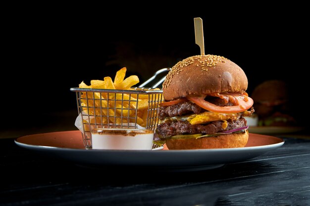 Köstlicher Burger mit Rindfleisch, Tomaten, Zwiebeln und gelber Sauce, serviert in einem roten Teller mit langsamem Cole-Salat. Amerikanisches Fast Food