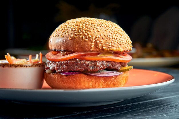 Köstlicher Burger mit Rindfleisch, Tomaten, Zwiebeln und gelber Soße, serviert in einem roten Teller mit Cole Slow Salad. Amerikanisches Fastfood