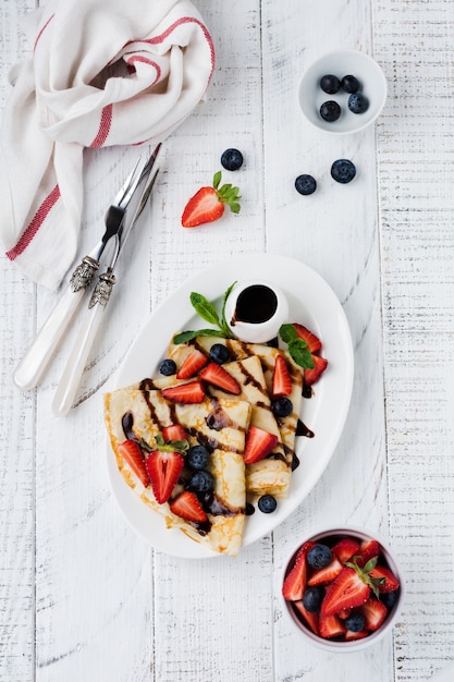 Köstlicher Crêpe mit Schokoladenüberzug und frischer Erdbeere auf weißem Teller, Draufsicht.