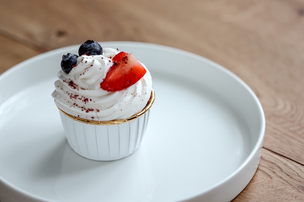 Köstlicher Cupcake mit Schlagsahne, frischer Erdbeere, Blaubeere auf weißem Teller.