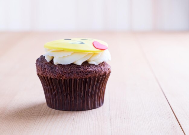 Köstlicher Cupcake mit Smiley-Symbol darauf auf einem Holzschreibtisch