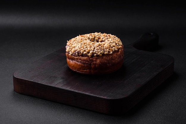 Köstlicher Donut mit Sahnefüllung und Nüssen auf dunklem Betonhintergrund