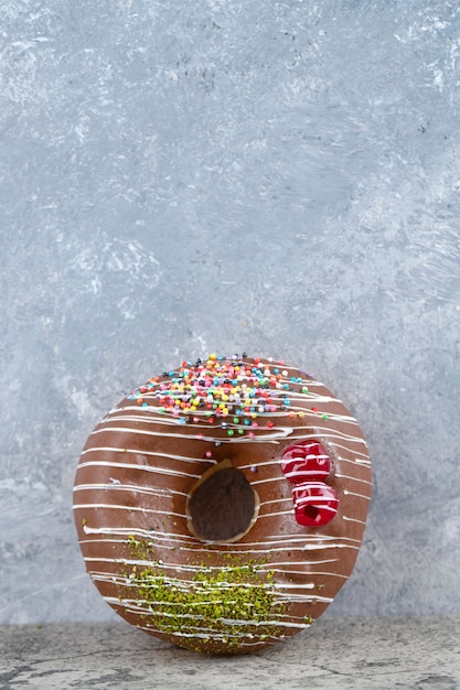 Köstlicher Donut mit Schokoladenglasur und Streuseln auf Steinhintergrund.