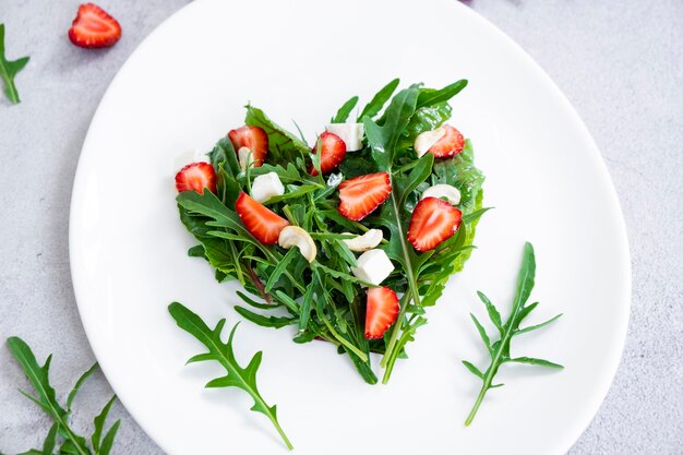 Köstlicher Erdbeersalat mit Kräutermischung, Rucola, Blattspinat, Feta-Käse und Cashewnüssen in Herzform auf weißem Teller. Vegetarisches Essen und Rohkost-Diät