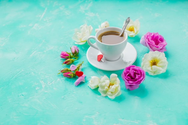 Köstlicher frischer Espressokaffee am Morgen mit einer schönen dicken Crema auf der azurblauen Tischwand mit nebligen Blasen, Rosenknospen darauf, flacher Kaffee, Rosenblüten