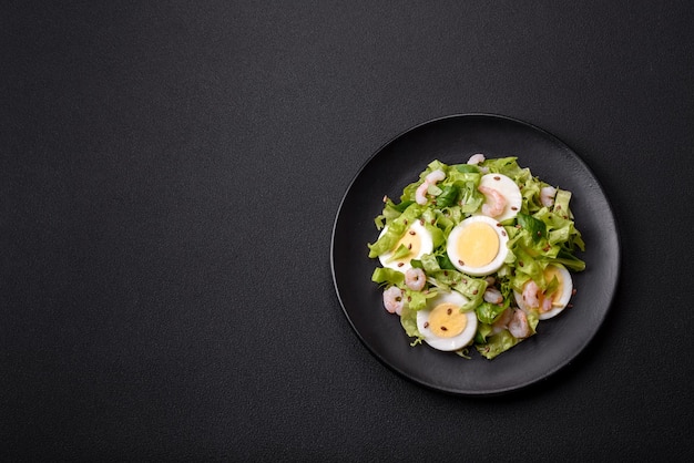 Köstlicher, frischer, gesunder Salat mit Garnelen-Eiersalat und Leinsamen auf einer schwarzen Keramikplatte auf Betongrund