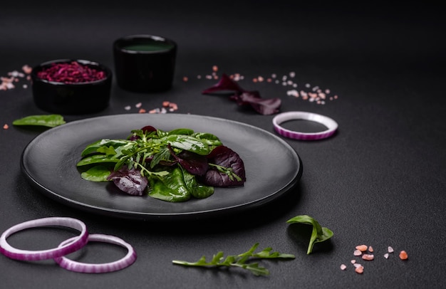 Köstlicher frischer Salat, bestehend aus Spinat Mangold Radicchio Red Chart Bulls Blood und Arugula auf einem schwarzen Teller auf dunklem Betongrund