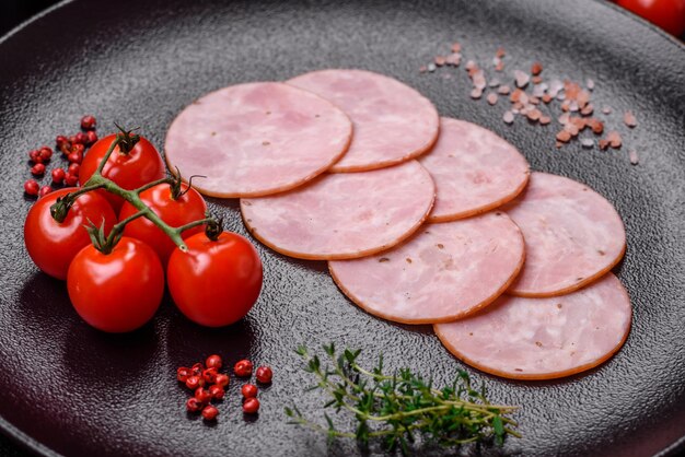 Köstlicher frischer Schinken, in runde Scheiben geschnitten, mit Salz, Gewürzen und Kräutern auf dunklem Betongrund