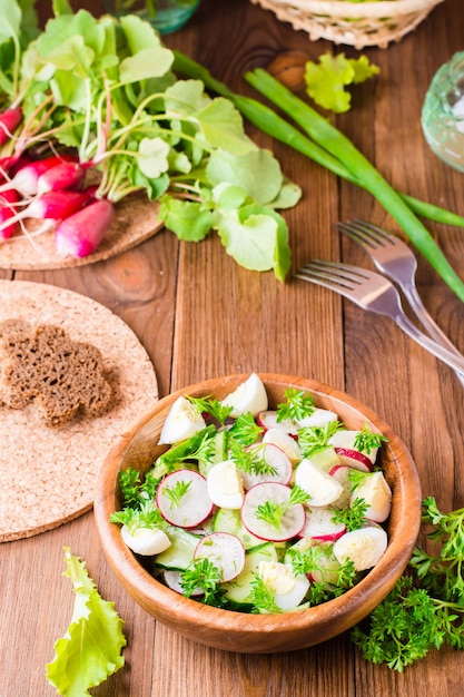 Köstlicher Frühlingsgemüsesalat von der Gurke, vom Rettich, von den Wachteleiern, von den Kräutern und vom Öl in einer Platte auf einem Holztisch