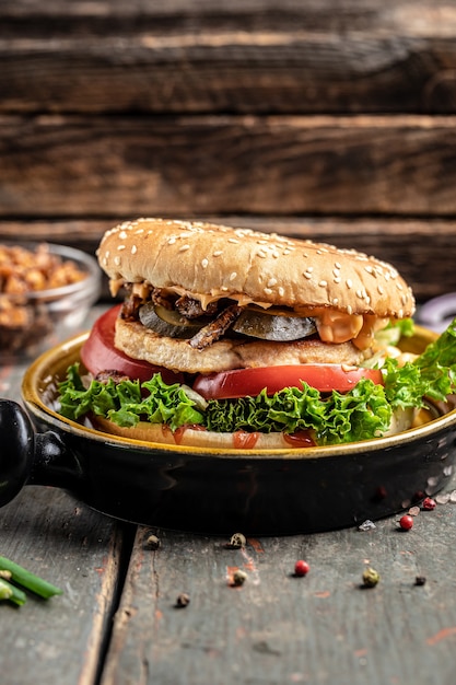 Köstlicher gegrillter Burger mit Hühnchen, Essiggurken und Röstzwiebeln. Rindfleischburger auf hölzernem Hintergrund. Fast-Food- und Junk-Food-Konzept