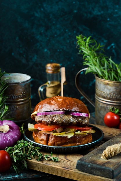 Köstlicher gegrillter Burger mit Kalbsschnitzel, Zwiebel und Gemüse auf dem alten dunklen Hintergrund