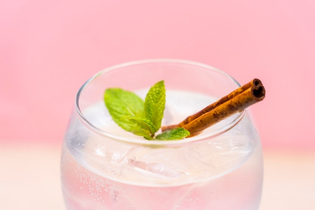 Köstlicher Gin Tonic Cocktail dekoriert mit Zimtschnecken Erdbeere und Minze auf rosa Hintergrund