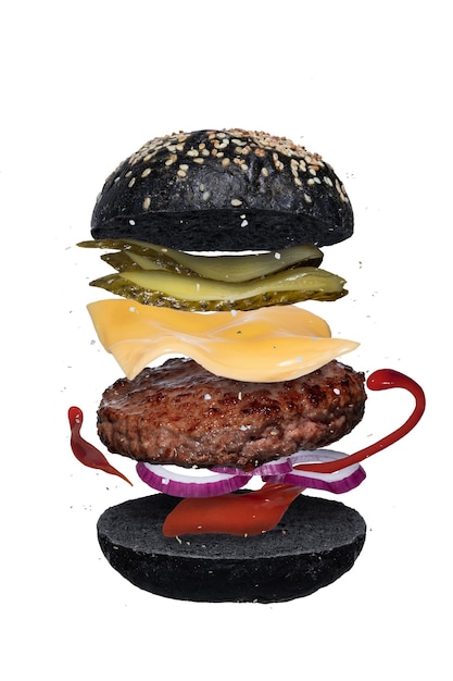 Köstlicher hamburger mit fliegenden bestandteilen über weißem hintergrund. schicht burger mit schwarzen tintenfischbrötchen, rinderschnitzel, käse, gurken, zwiebeln und tomatensauce oder ketchup isoliert