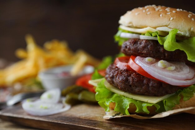 Köstlicher hausgemachter Burger mit Pommes-Frites-Tomaten-Salat-Zwiebeln-Käse auf rustikalem Tisch