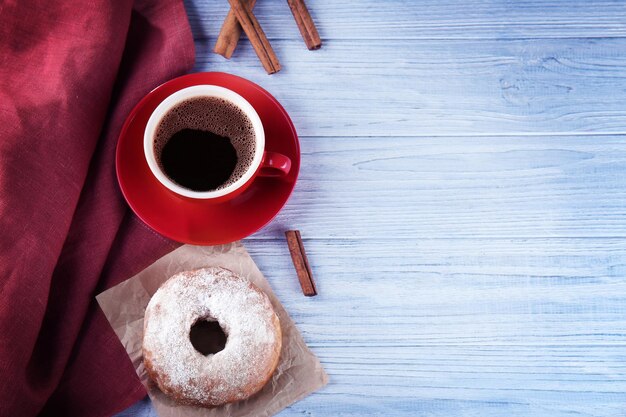 Köstlicher hausgemachter Donut mit Zuckerpulver und einer Tasse Kaffee auf Holzhintergrund