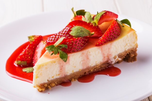 Köstlicher hausgemachter Käsekuchen mit Erdbeeren auf weißem Holztisch.