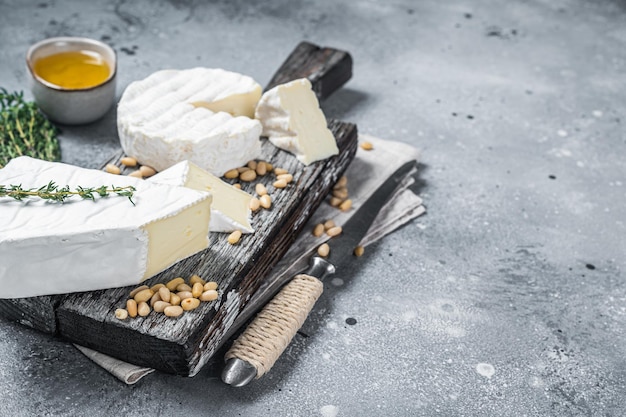 Köstlicher Käsebrie und Camembert auf Holzbrett mit Kräutern und Nüssen Französische Molkereiprodukte Grauer Hintergrund Draufsicht Kopierbereich