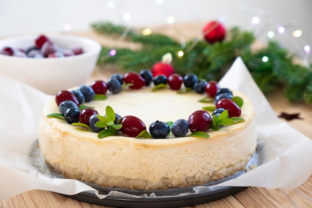 Köstlicher Käsekuchen verziert mit Blaubeere und Cranberry mit Tannenzweigen in Weihnachtsbeleuchtung Bokeh im Hintergrund. Rezept für festlichen Kuchen für das Neujahrs- und Weihnachtsmenü.