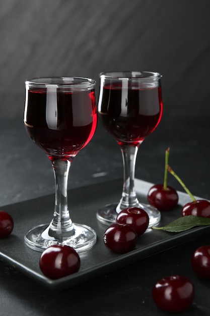 Köstlicher Kirschlikör in Gläsern und Beeren auf schwarzem Tisch in Nahaufnahme