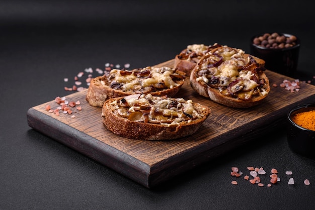 Köstlicher knuspriger Toast oder Bruschetta mit gebratenen Zwiebelchampignons und Käse mit Gewürzen und Kräutern auf dunklem Betonhintergrund