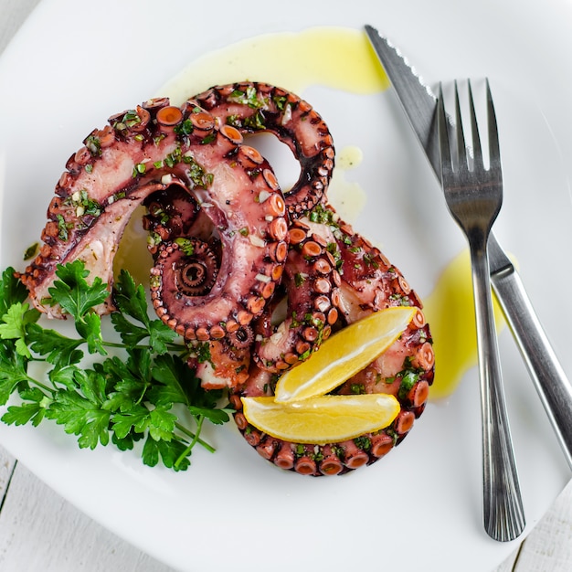 Köstlicher Krakensalat mit dem Kleiden, Zitrone und Petersilie auf weißem Hintergrund. Gesundes Essen. Meeresfrüchte kochen