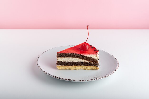 Köstlicher Kuchen mit Kirschen auf weißem Teller auf rosa Hintergrund.