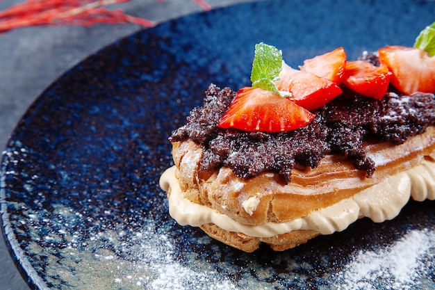 Köstlicher Kuchen Profiteroles mit Trüffelpaste, Pudding und Erdbeeren auf dunklem Teller. Dessert zum Mittagessen. Bäckerei. Lebensmittelfoto für Menü oder Rezept