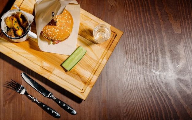 Köstlicher leckerer Burger mit Salat, Käse, Zwiebel und Tomate auf einem rustikalen Holzbrett auf Schwarz