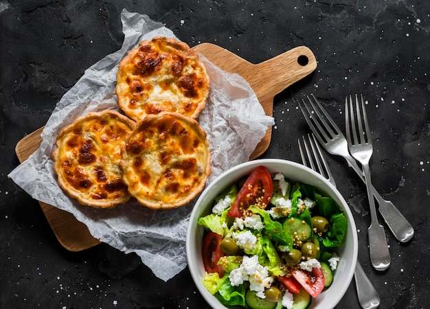 Köstlicher Mittagstisch Mini-Thunfisch-Mozzarella-Quiche und frischer griechischer Salat auf dunklem Hintergrund Draufsicht