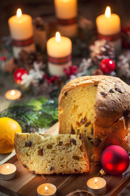 Köstlicher Panettone auf Weihnachtstisch mit Dekorationen und Adventskranz und Kerzen.