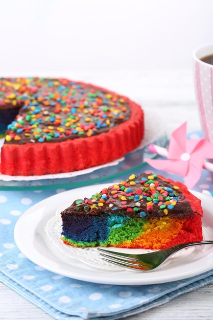 Köstlicher Regenbogenkuchen auf Teller auf Tisch auf hellem Hintergrund