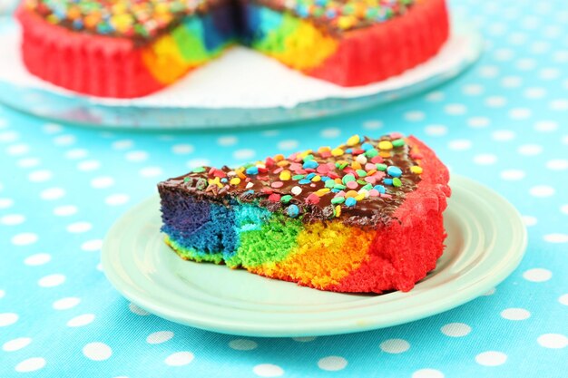 Köstlicher Regenbogenkuchen auf Teller auf Tischdeckenhintergrund