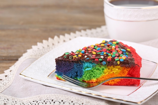 Köstlicher Regenbogenkuchen auf Teller und Tasse mit heißem Getränk auf Holzhintergrund