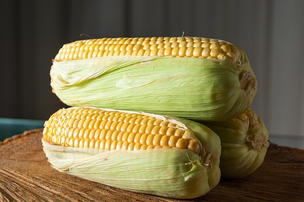 Köstlicher roher gelber Mais mit grünem Blatt und Maiskolben über trockenen Strohhalmen und Holzoberfläche