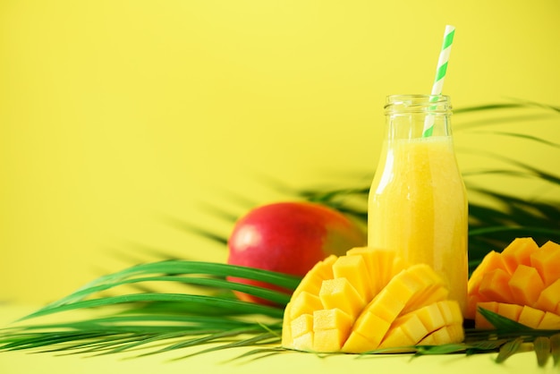 Köstlicher saftiger Smoothie mit Orangenfrucht und Mango. Frischer Saft in Glasflaschen über grünen Palmblättern.