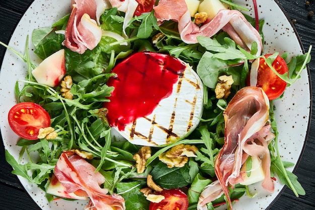 Foto köstlicher salat mit gegrilltem camembert, rucola, spinat, jamon, kirschtomaten in weiß auf schwarz