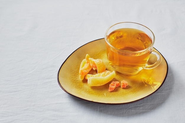 Köstlicher schwarzer Tee in Glasschale und kandierten Früchten auf gelber Untertasse