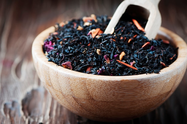 Köstlicher schwarzer Tee mit Blütenblättern auf dem Holztisch