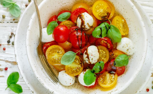 Köstlicher Sommersalat aus gelben und roten Kirschtomaten, Mozzarella mit Basilikum und Gewürzen