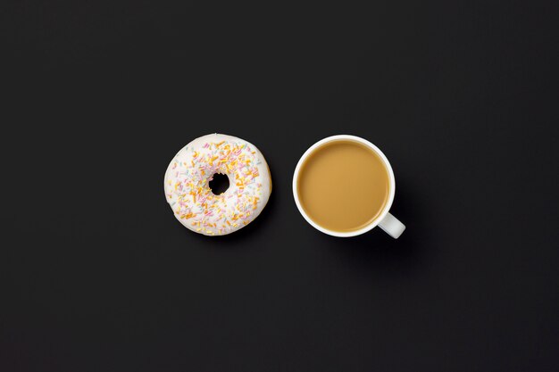 Köstlicher, süßer, frischer Donut, Tasse Kaffee, schwarzer Hintergrund. Konzept von Frühstück, Fast Food, Café, Bäckerei. Minimalismus. Flache Lage, Draufsicht.