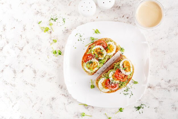 Köstlicher Toast mit Avocado, gekochten Eiern, Tomaten und Mikrogreen auf einem weißen Teller, gesundes Frühstück, Keto-Diät, trendiges Essen, Top-View