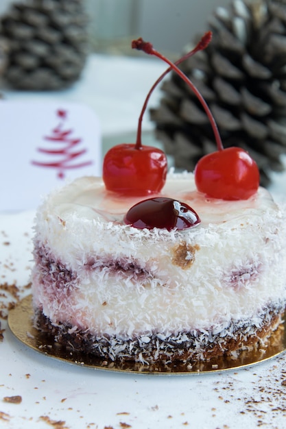 Köstlicher Winter-Kokos-/Kirschkuchen mit einer Grußkarte auf weißem Hintergrund und Tannenzapfen im Hintergrund