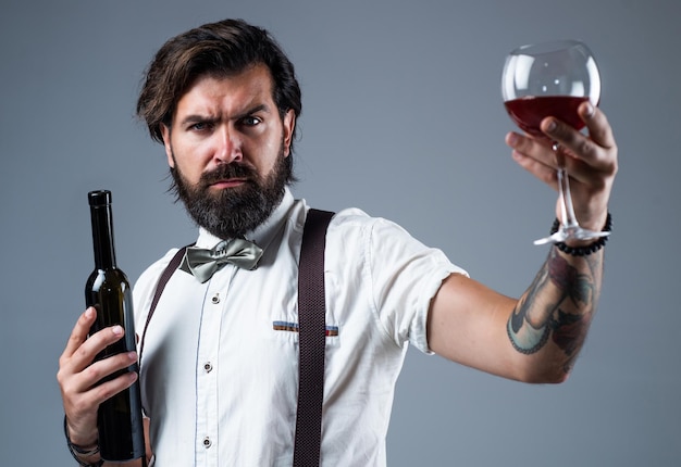 Köstliches alkoholisches Getränk stilvoller Sommelier-Getränk altmodischer bärtiger Hipster-Winzer trendiger Mann in Hosenträgern und Fliege mit Wein selbstbewusster eleganter Mann, der Wein aus Glas trinkt