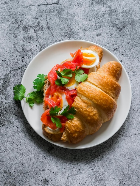 Köstliches Brunch-Frühstücks-Snack-Croissant-Sandwich mit Frischkäse-Lachs und gekochtem Ei auf hellem Hintergrund, Draufsicht