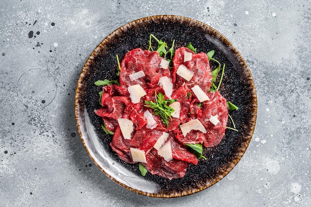 Köstliches Carpaccio vom Kalb mit Parmesan-Käse-Gewürzen und Kräutern Grauer Hintergrund Ansicht von oben