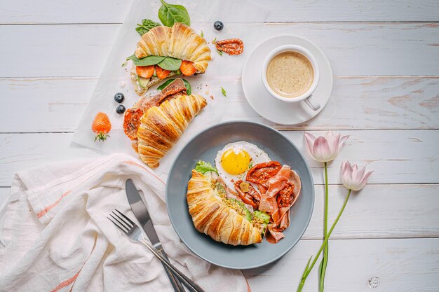 Köstliches Croissant-Frühstück gefüllt mit Ricotta und Avocado mit sonnengetrockneten Tomatenstückchen Jamon-Spiegelei